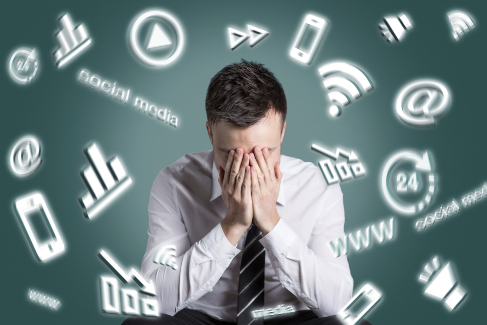 SNSの様々なアイコンとパソコンの前で顔を手で覆っている男性